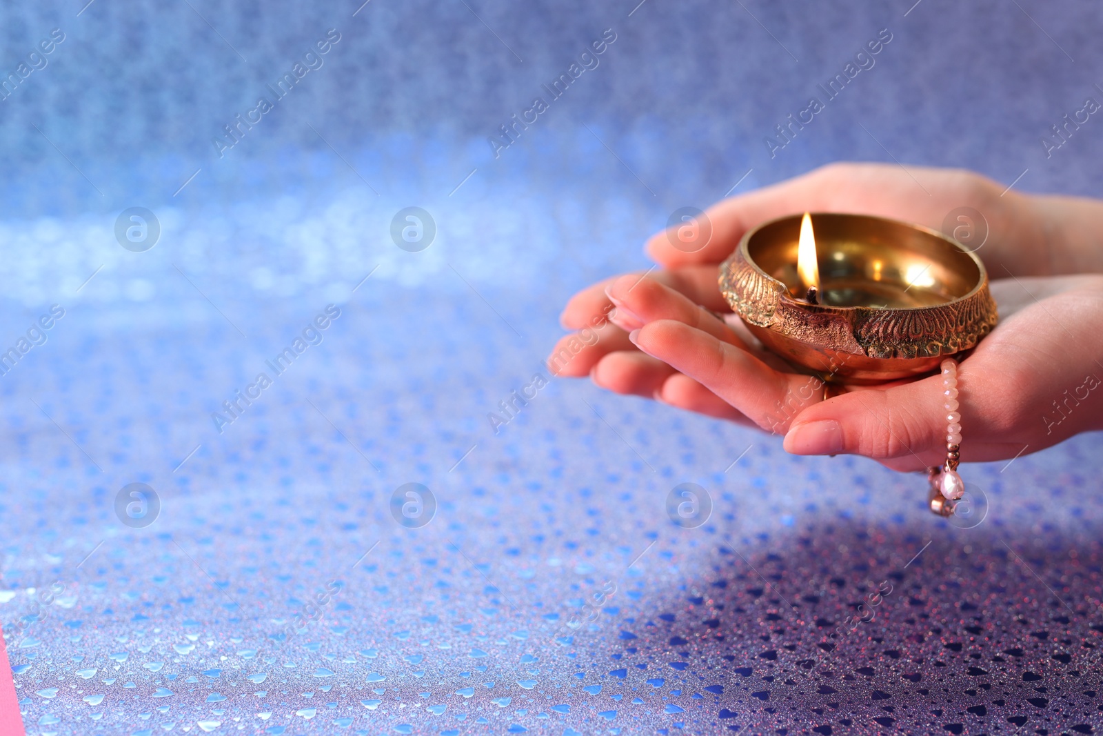 Photo of Diwali celebration. Woman holding lit diya lamp on color background, closeup. Space for text