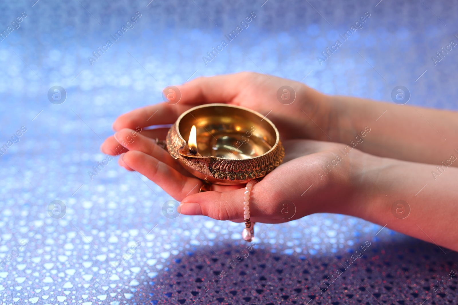 Photo of Diwali celebration. Woman holding lit diya lamp on color background, closeup