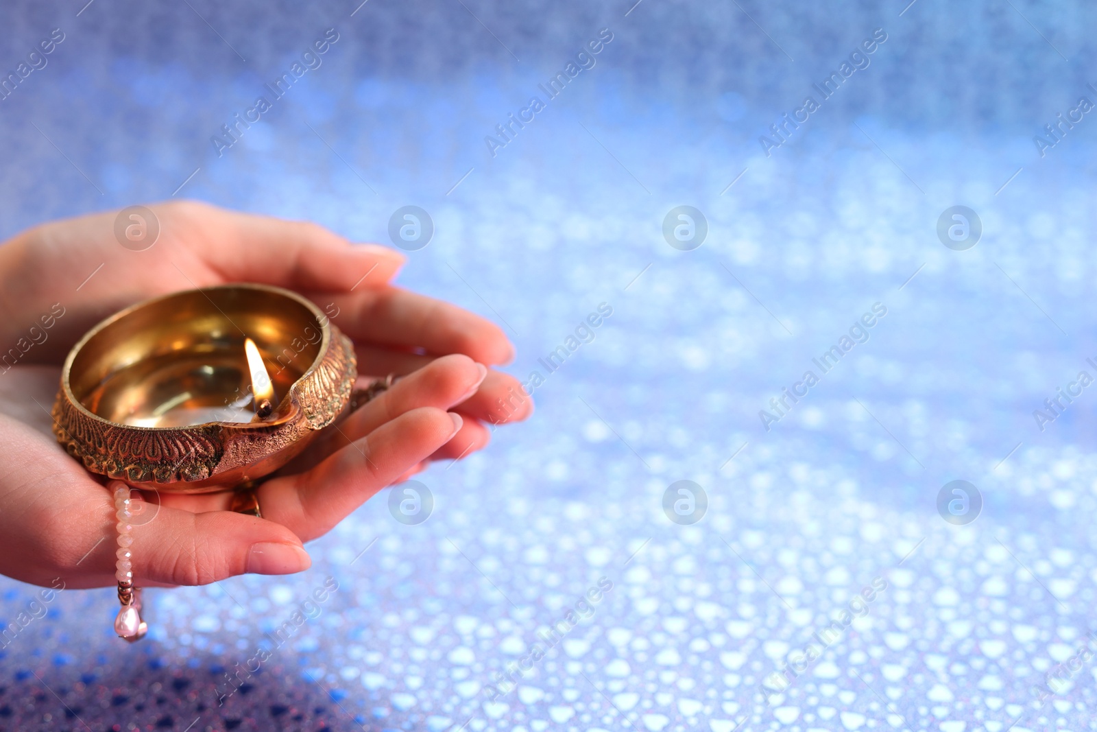 Photo of Diwali celebration. Woman holding lit diya lamp on color background, closeup. Space for text