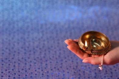 Photo of Diwali celebration. Woman holding lit diya lamp on color background, closeup. Space for text