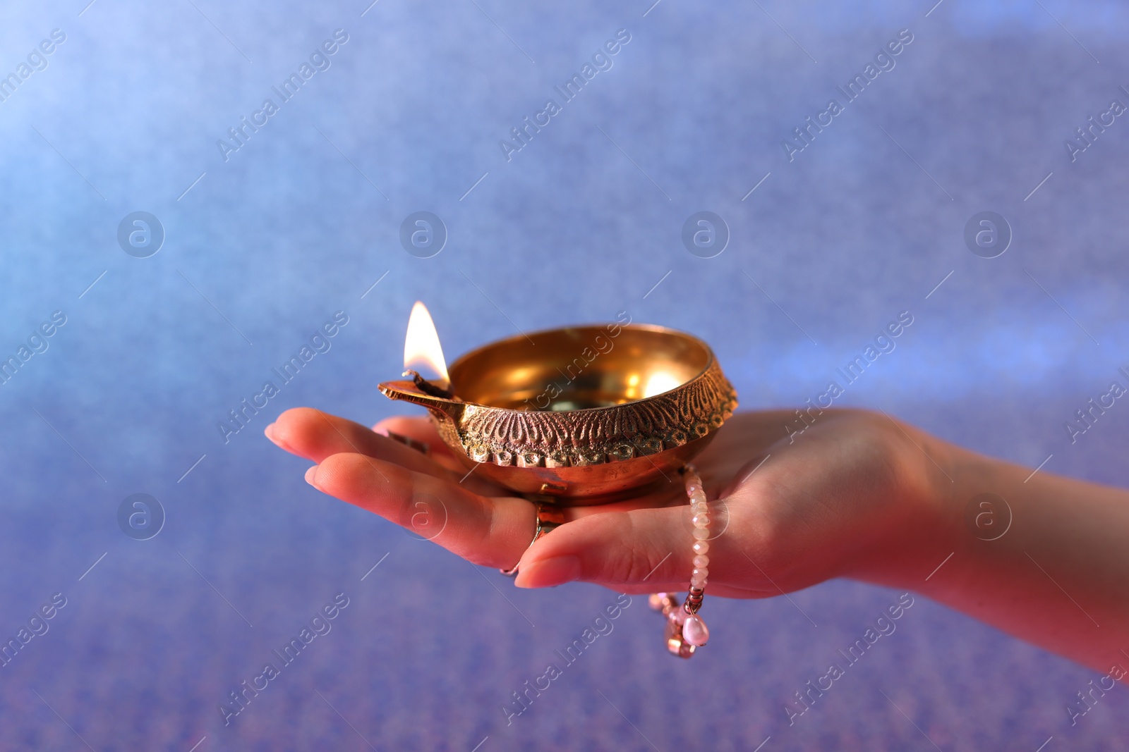 Photo of Diwali celebration. Woman holding lit diya lamp on color background, closeup