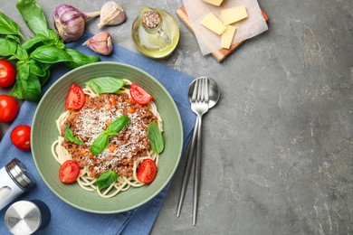 Delicious pasta bolognese with basil and tomatoes served on grey table, flat lay. Space for text