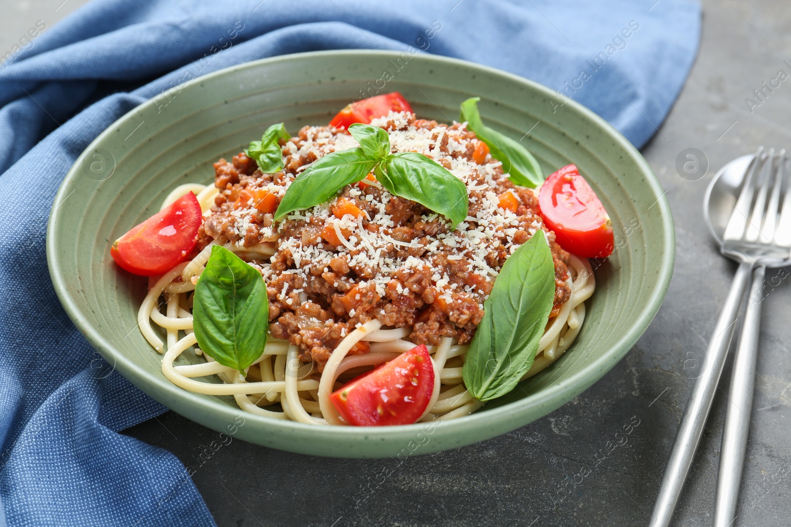 Photo of Delicious pasta bolognese with basil and tomatoes served on grey table, closeup