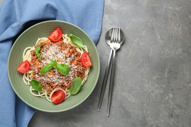 Photo of Delicious pasta bolognese with basil and tomatoes served on grey table, top view. Space for text