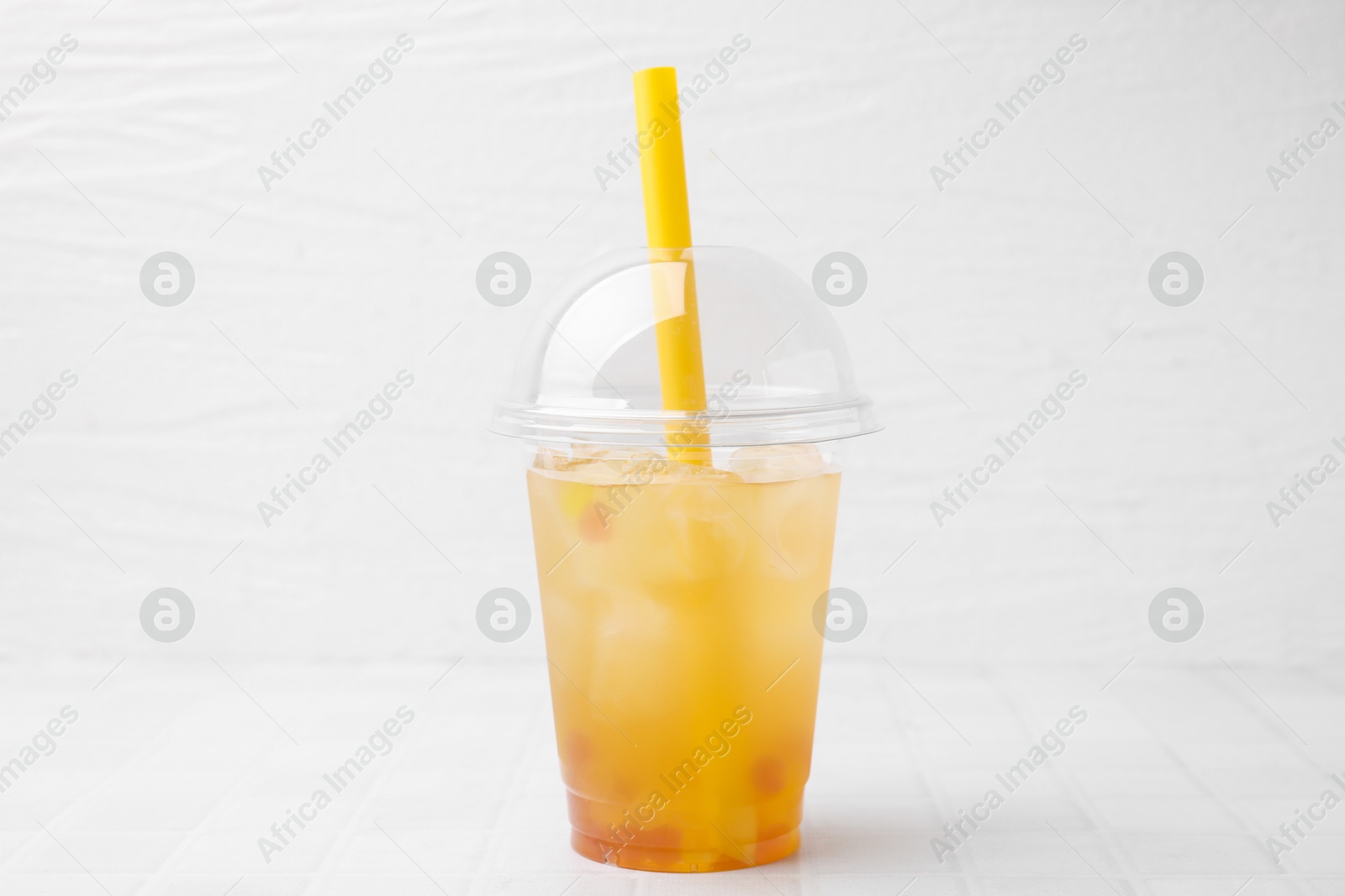 Photo of Tasty bubble tea in plastic cup on white tiled table against light background