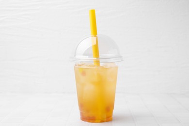 Photo of Tasty bubble tea in plastic cup on white tiled table against light background