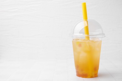 Photo of Tasty bubble tea in plastic cup on white tiled table against light background, space for text