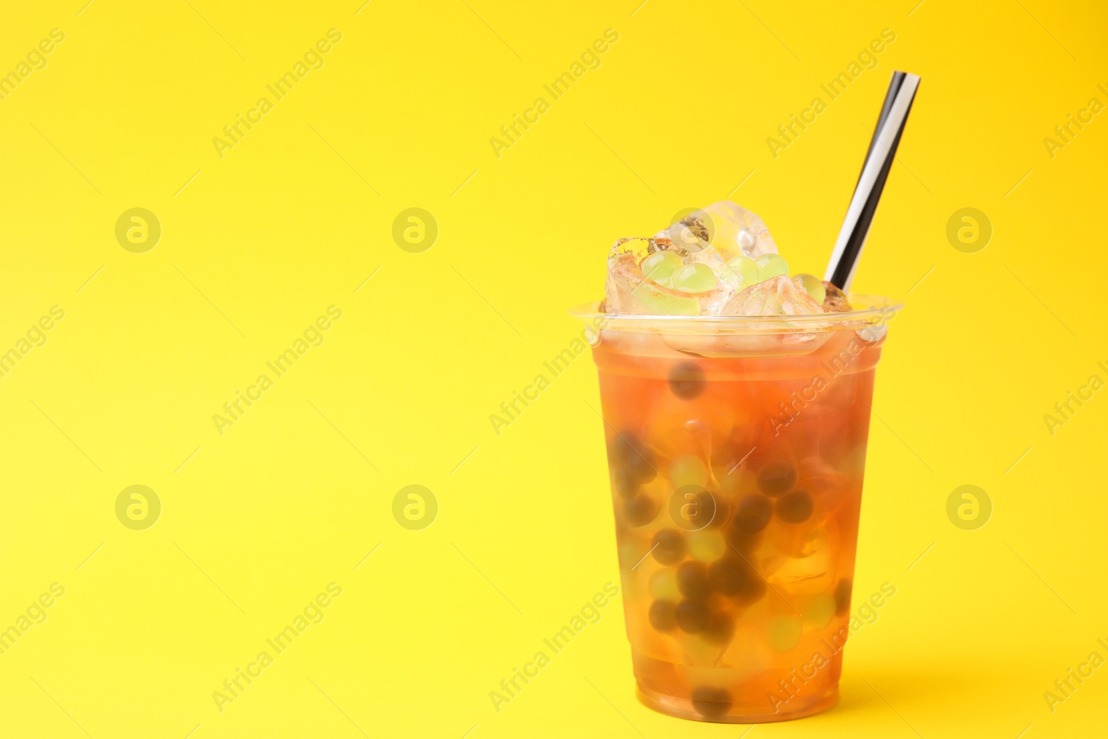 Photo of Tasty bubble tea in plastic cup on yellow background, space for text