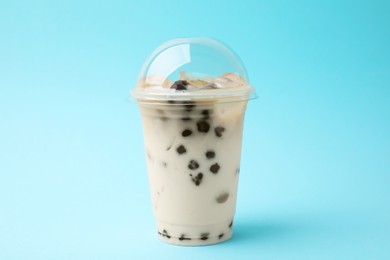 Photo of Tasty milk bubble tea in plastic cup on light blue background