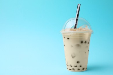 Photo of Tasty milk bubble tea in plastic cup on light blue background, space for text