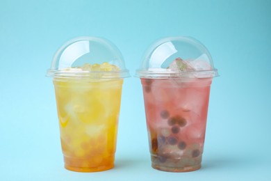 Photo of Tasty bubble tea in plastic cups on light blue background