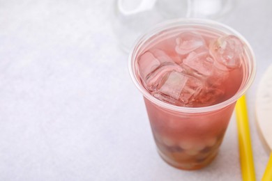 Photo of Tasty bubble tea in plastic cup on light table, closeup. Space for text