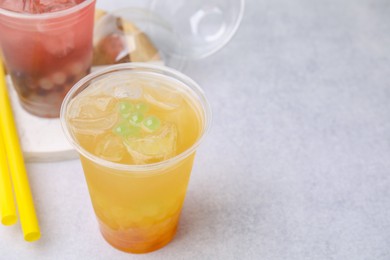 Photo of Tasty bubble tea in plastic cups and straws on light table, closeup. Space for text