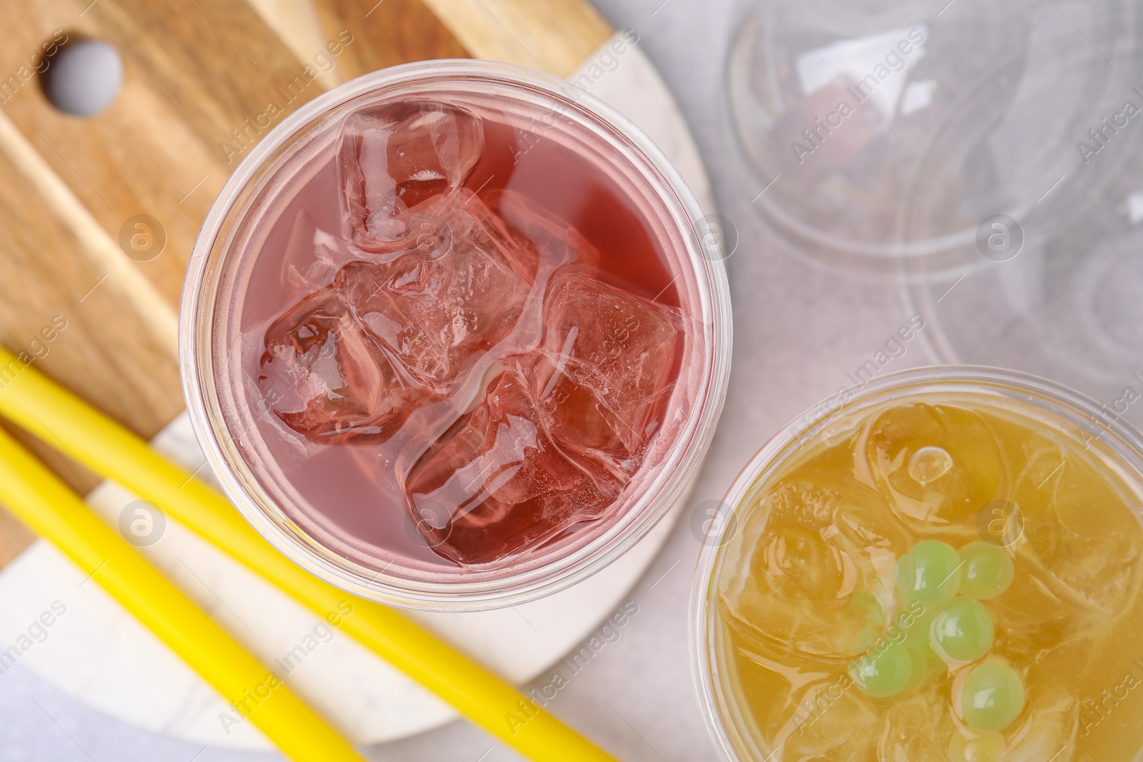 Photo of Tasty bubble tea in plastic cups and straws on light table, flat lay