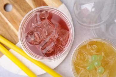 Photo of Tasty bubble tea in plastic cups and straws on light table, flat lay