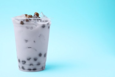 Photo of Tasty milk bubble tea in plastic cup on light blue background, space for text