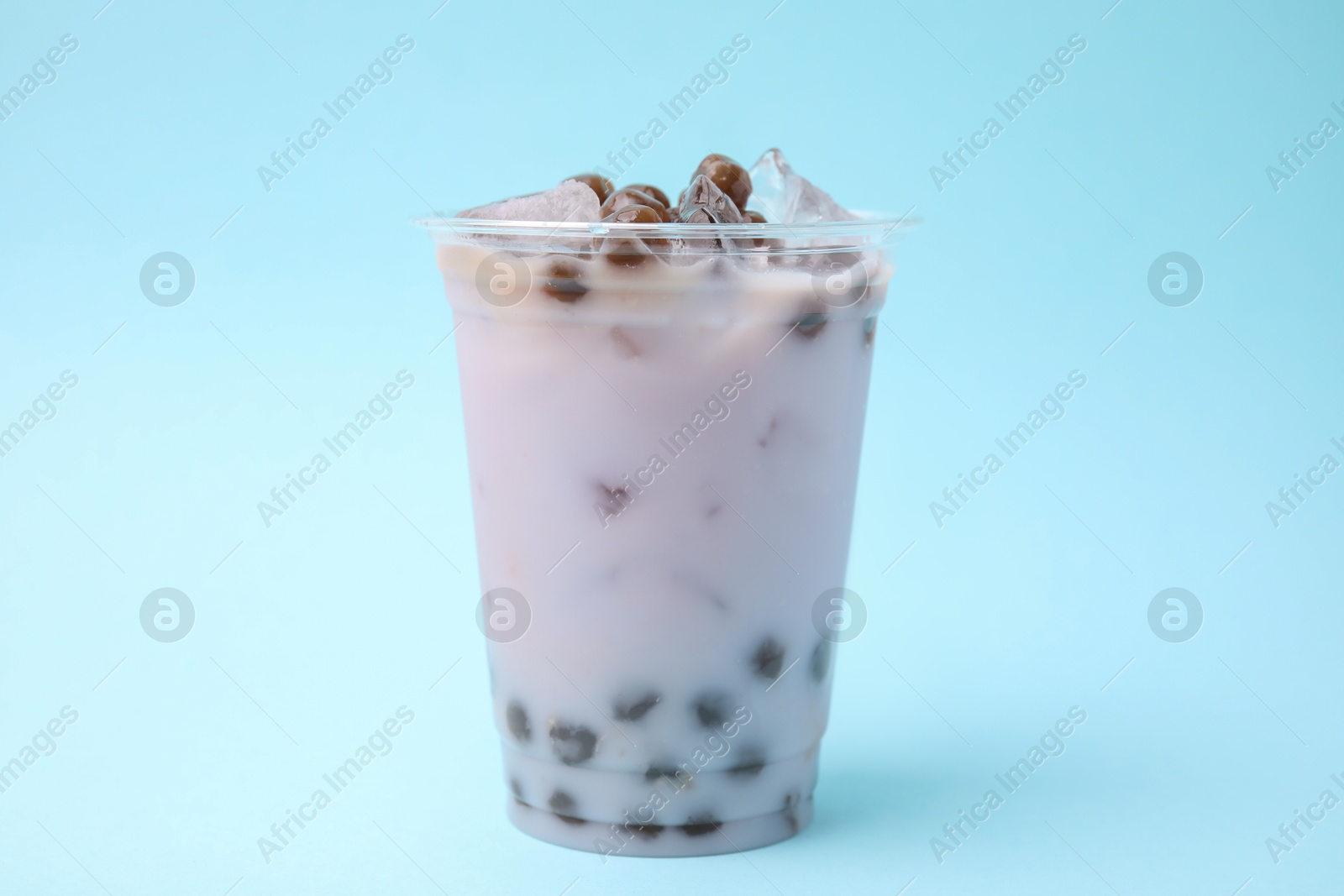 Photo of Tasty milk bubble tea in plastic cup on light blue background