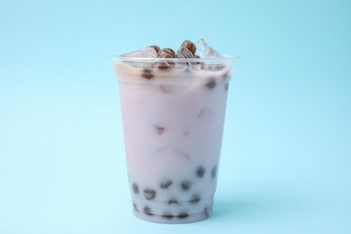 Photo of Tasty milk bubble tea in plastic cup on light blue background