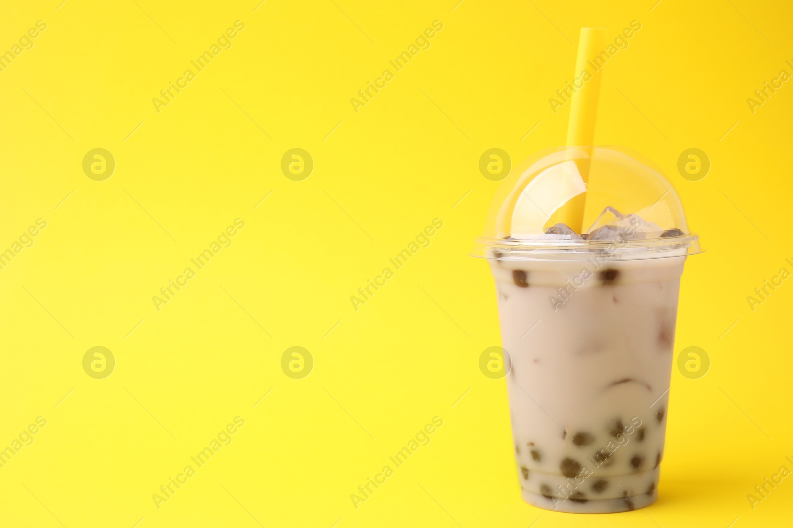 Photo of Tasty milk bubble tea in plastic cup on yellow background, space for text