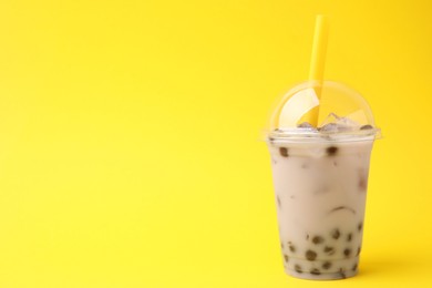 Photo of Tasty milk bubble tea in plastic cup on yellow background, space for text