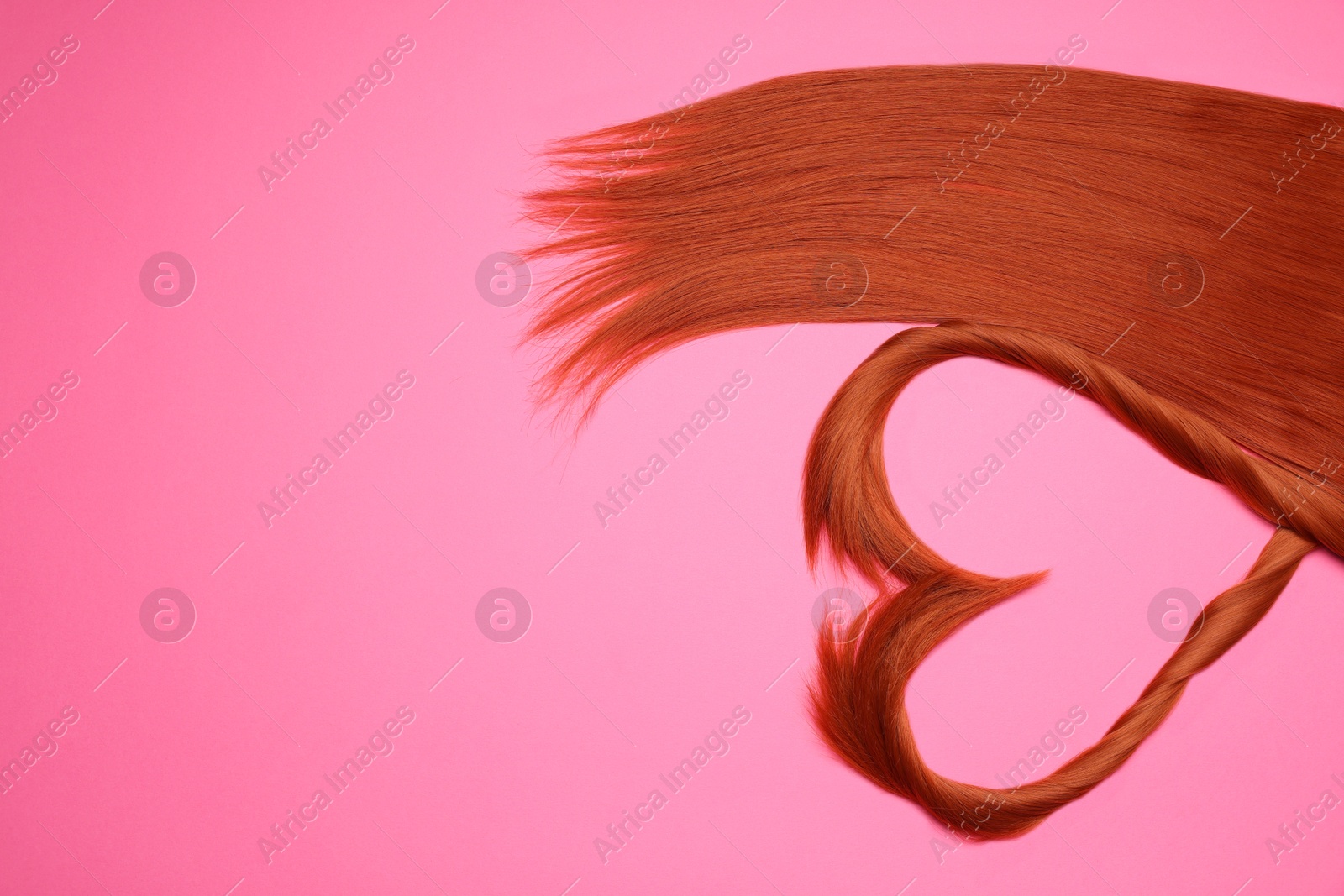 Photo of Red hair strands in shape of heart on pink background, top view. Space for text