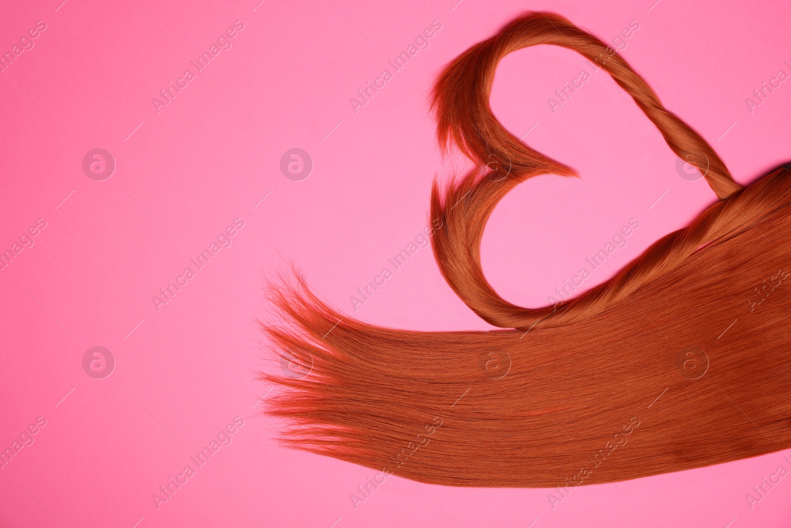 Photo of Red hair strands in shape of heart on pink background, top view. Space for text