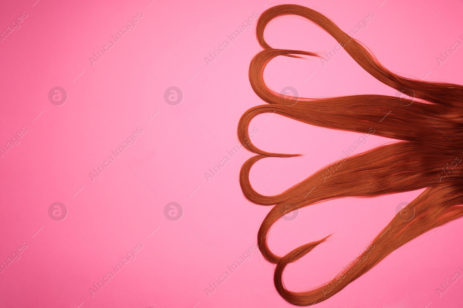 Photo of Red hair strands in shape of hearts on pink background, top view. Space for text