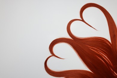 Photo of Red hair strands in shape of hearts on white background, top view. Space for text