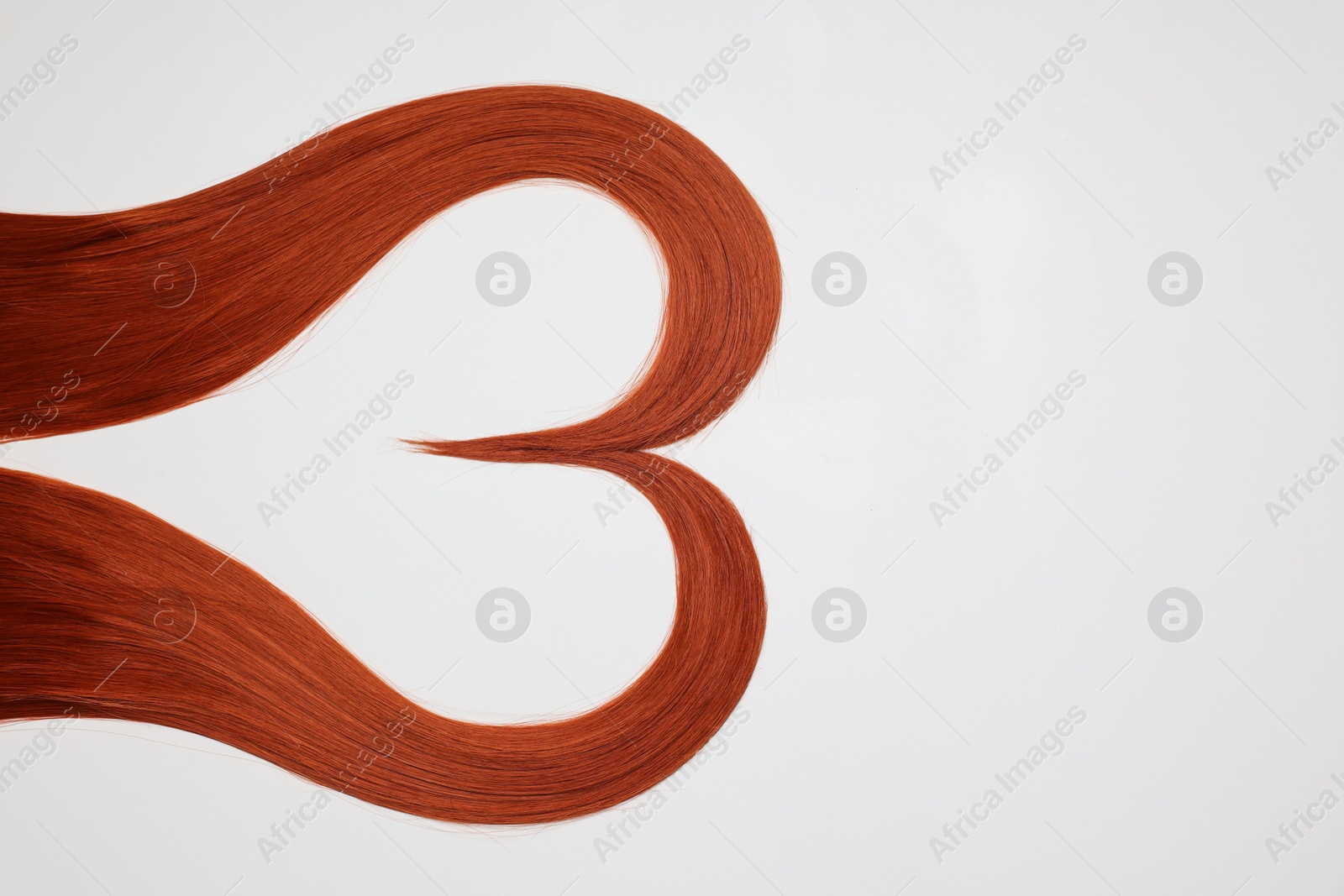 Photo of Red hair strands in shape of heart on white background, top view. Space for text