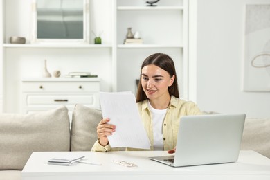 Photo of Budget planning. Beautiful young woman with papers and laptop indoors