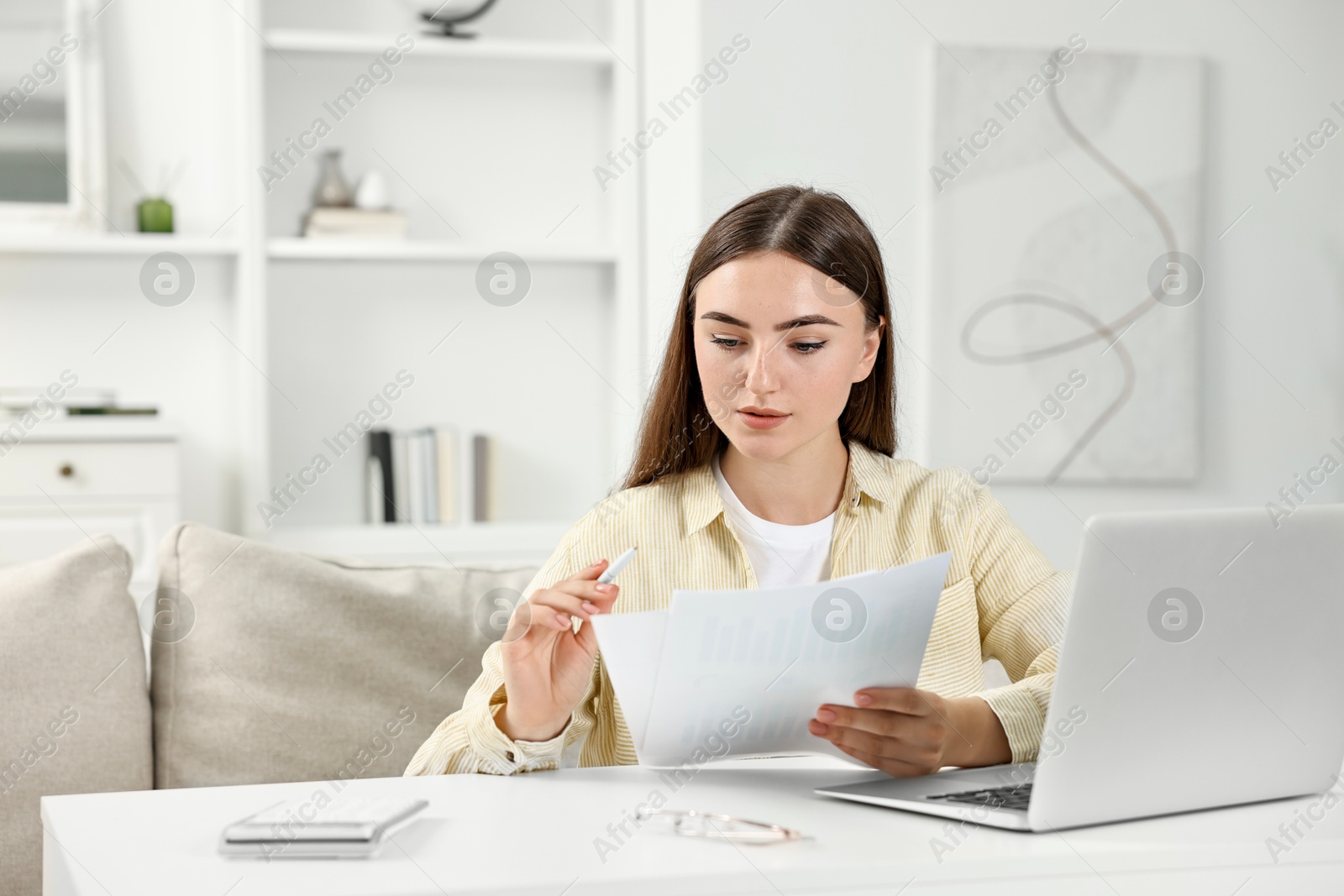 Photo of Budget planning. Beautiful young woman with papers and laptop indoors