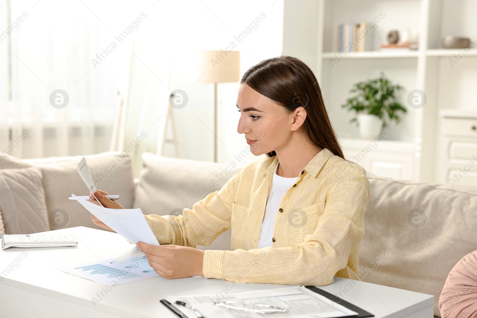 Photo of Budget planning. Beautiful young woman with papers at white table indoors