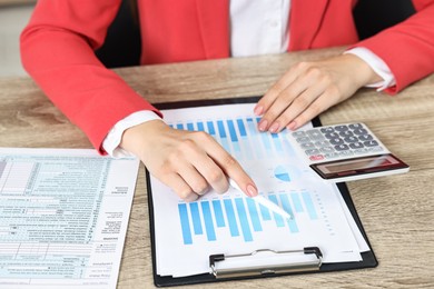 Photo of Budget planning. Woman with papers and calculator at wooden table, closeup