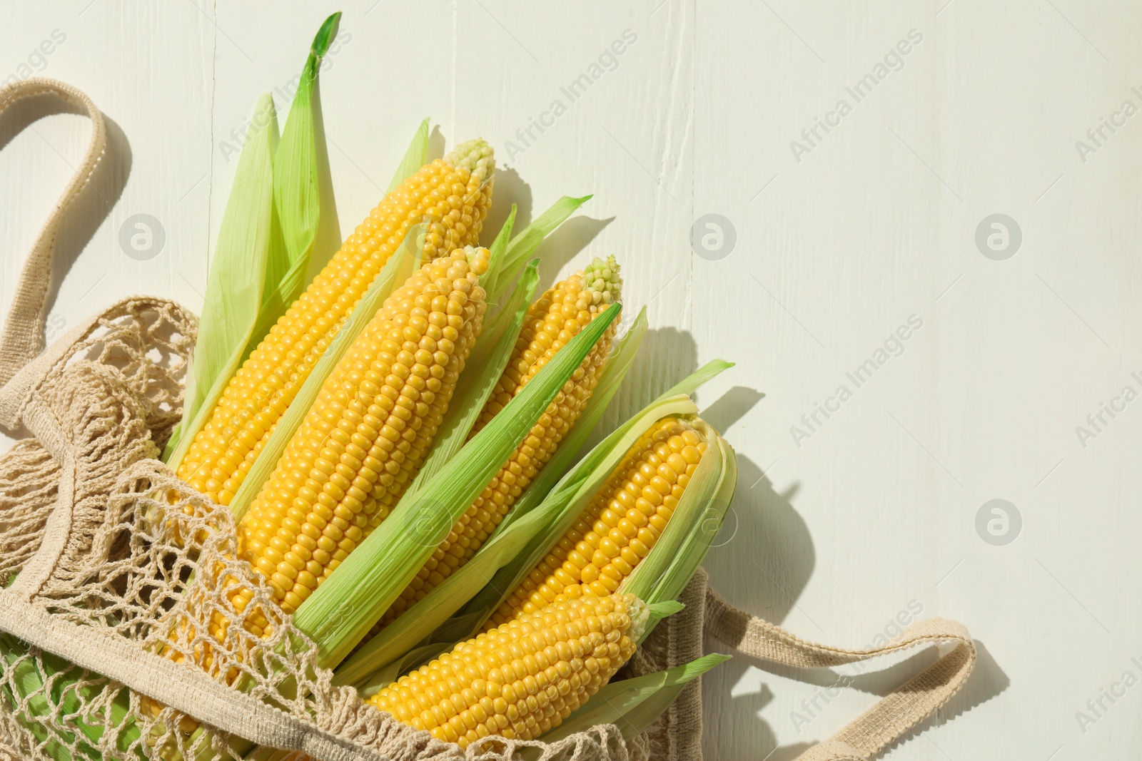 Photo of Many fresh ripe corncobs with green husks on white wooden table, top view. Space for text