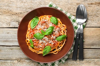 Photo of Delicious pasta bolognese with basil and cutlery on wooden table, top view