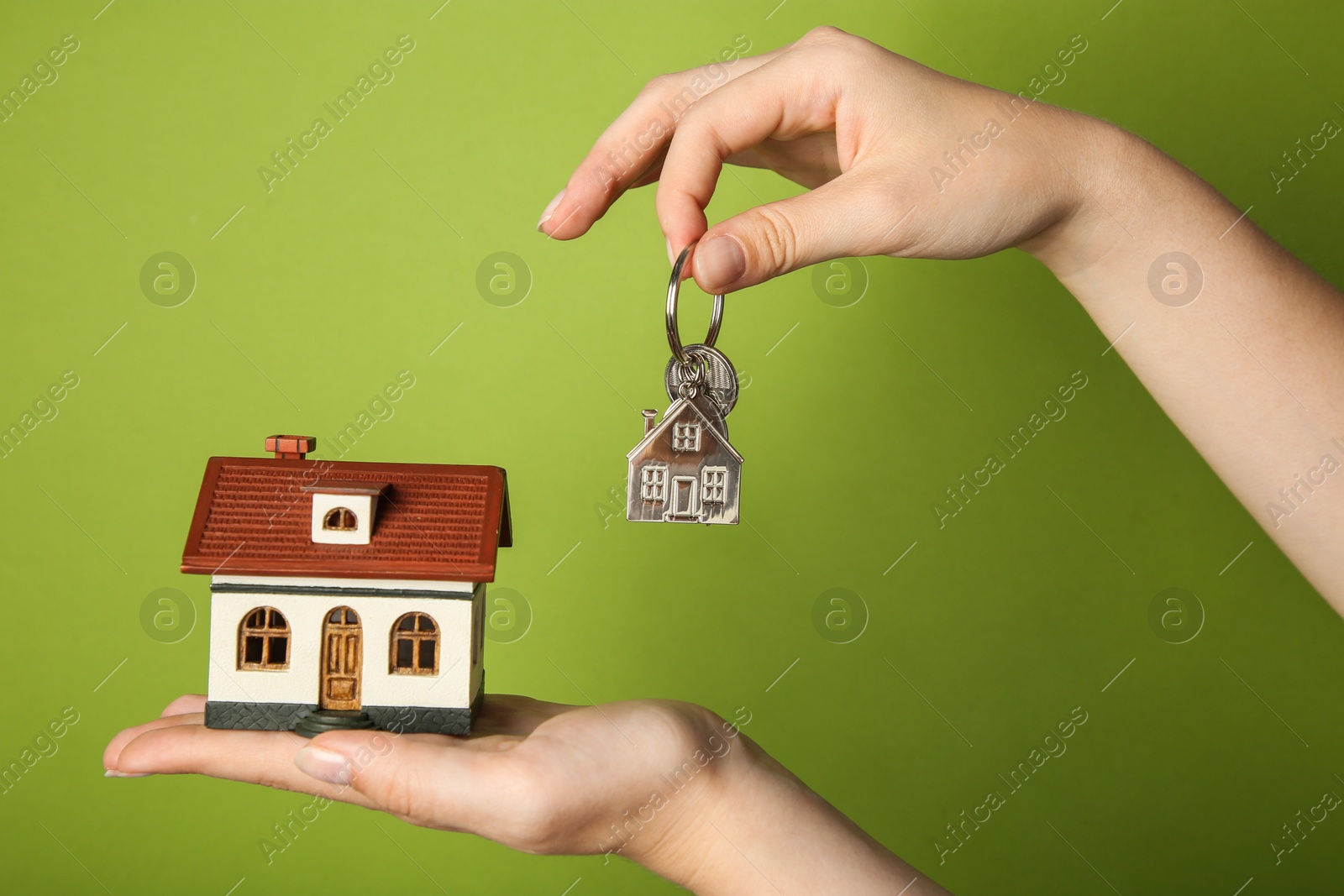 Photo of Woman with house model and key on green background, closeup