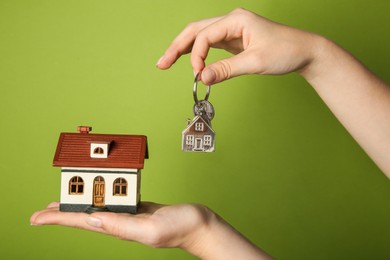 Photo of Woman with house model and key on green background, closeup