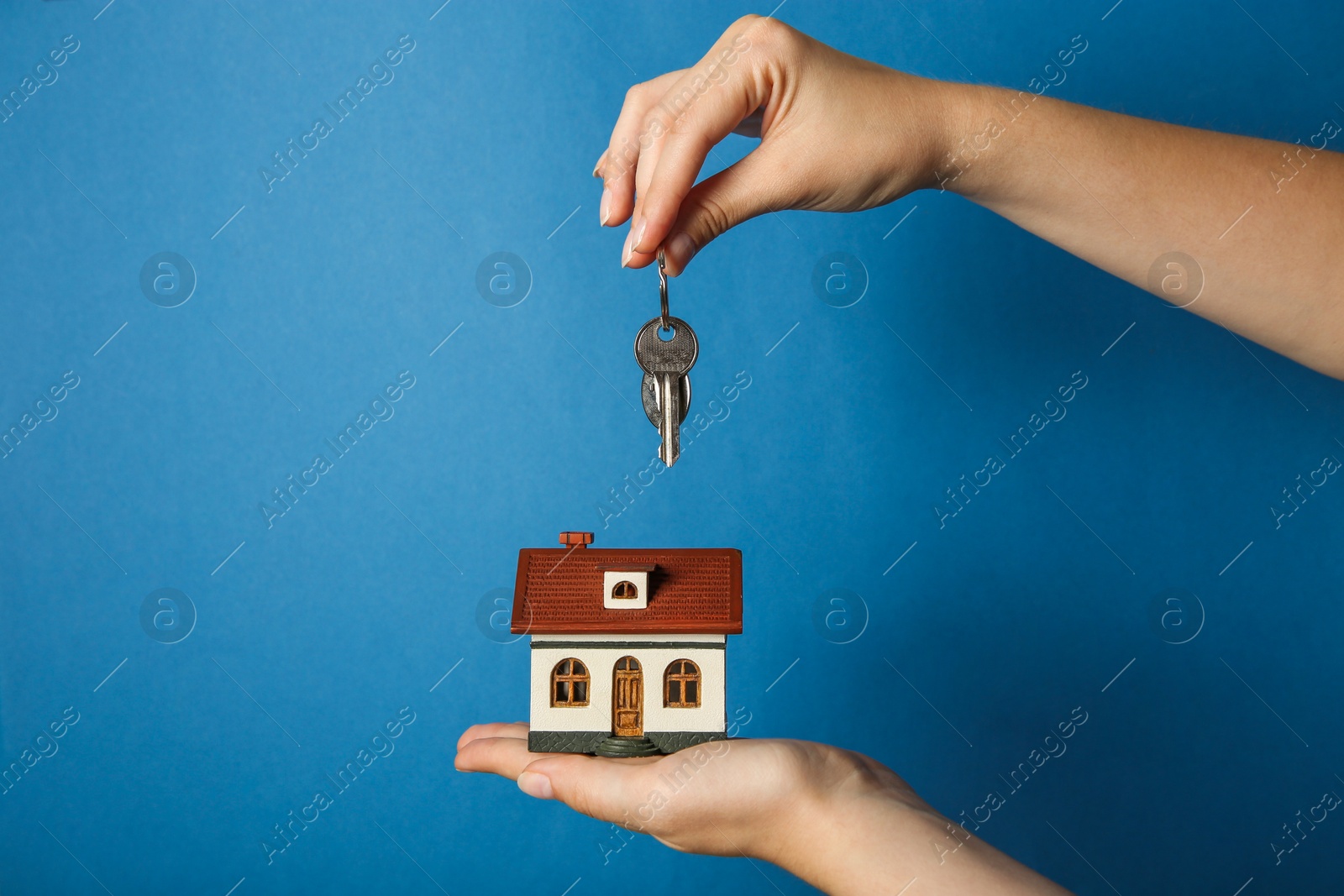 Photo of Woman with house model and key on light blue background, closeup