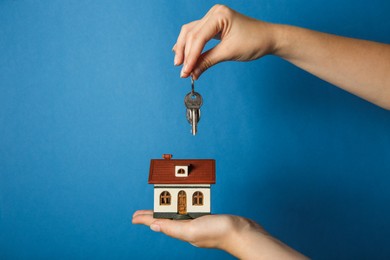 Woman with house model and key on light blue background, closeup