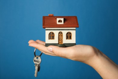 Photo of Woman with house model and key on light blue background, closeup