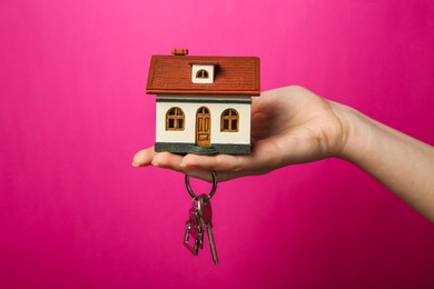 Woman with house model and key on pink background, closeup