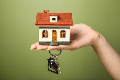 Woman with house model and key on olive background, closeup