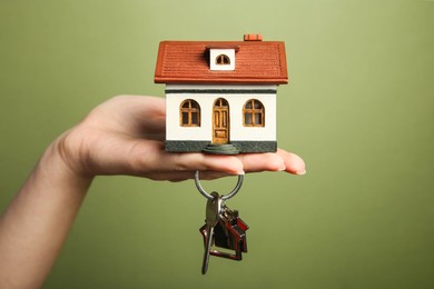 Photo of Woman with house model and key on olive background, closeup