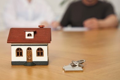 Photo of House model and key on wooden table indoors, selective focus