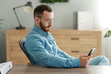 Photo of Handsome man looking at smartphone in office