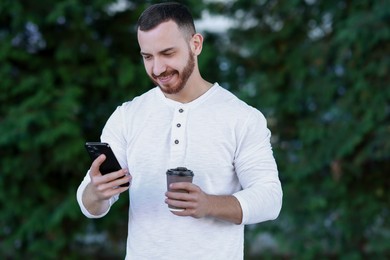 Photo of Happy man with paper cup using smartphone on blurred background