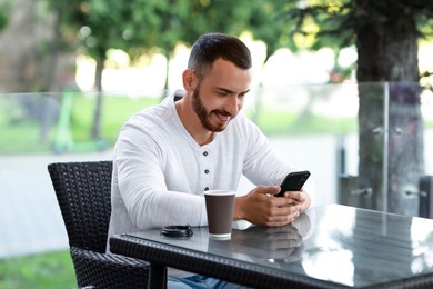 Happy man with paper cup using smartphone at outdoor cafe