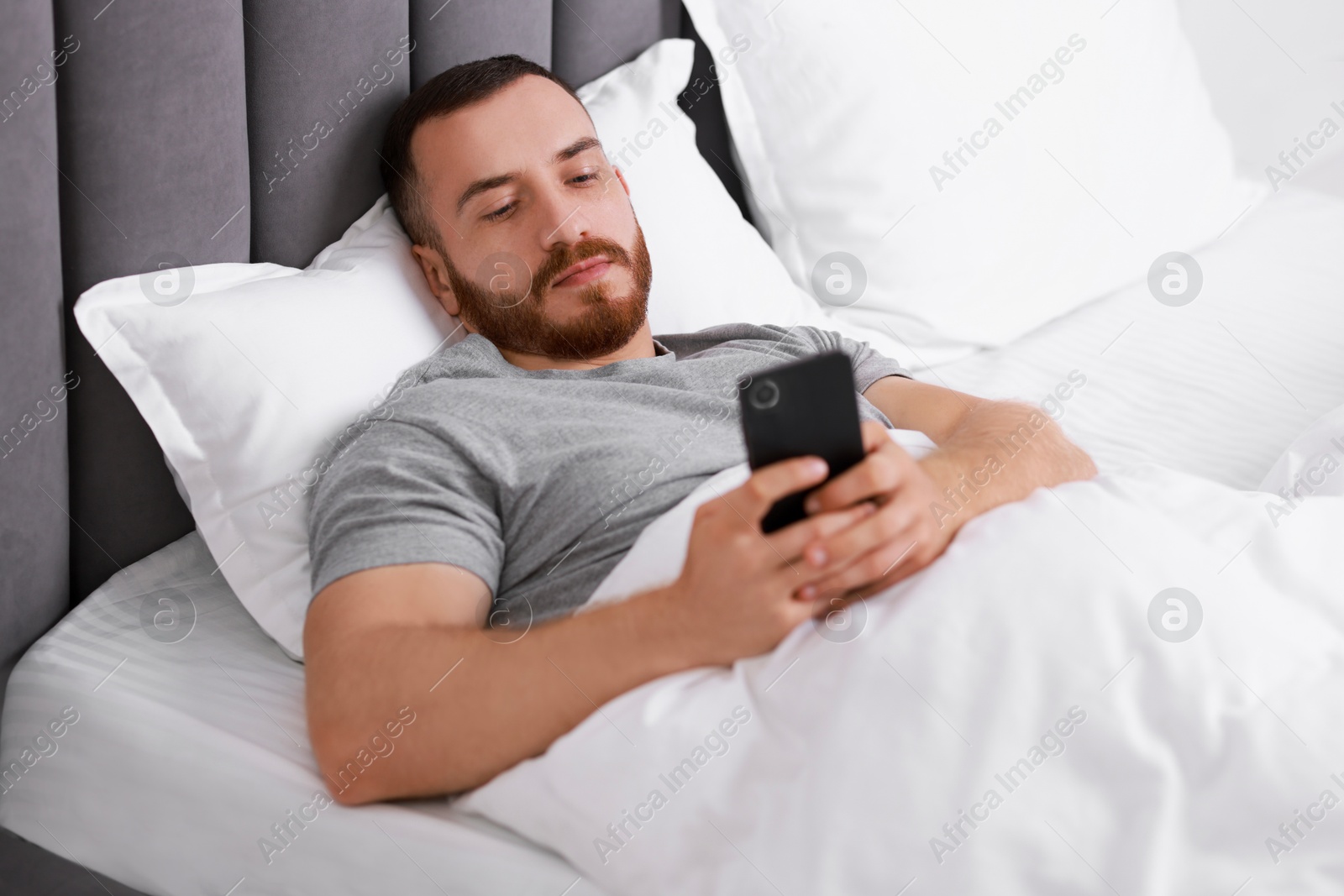 Photo of Handsome man using mobile phone in bed