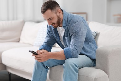 Photo of Handsome man using smartphone on sofa indoors