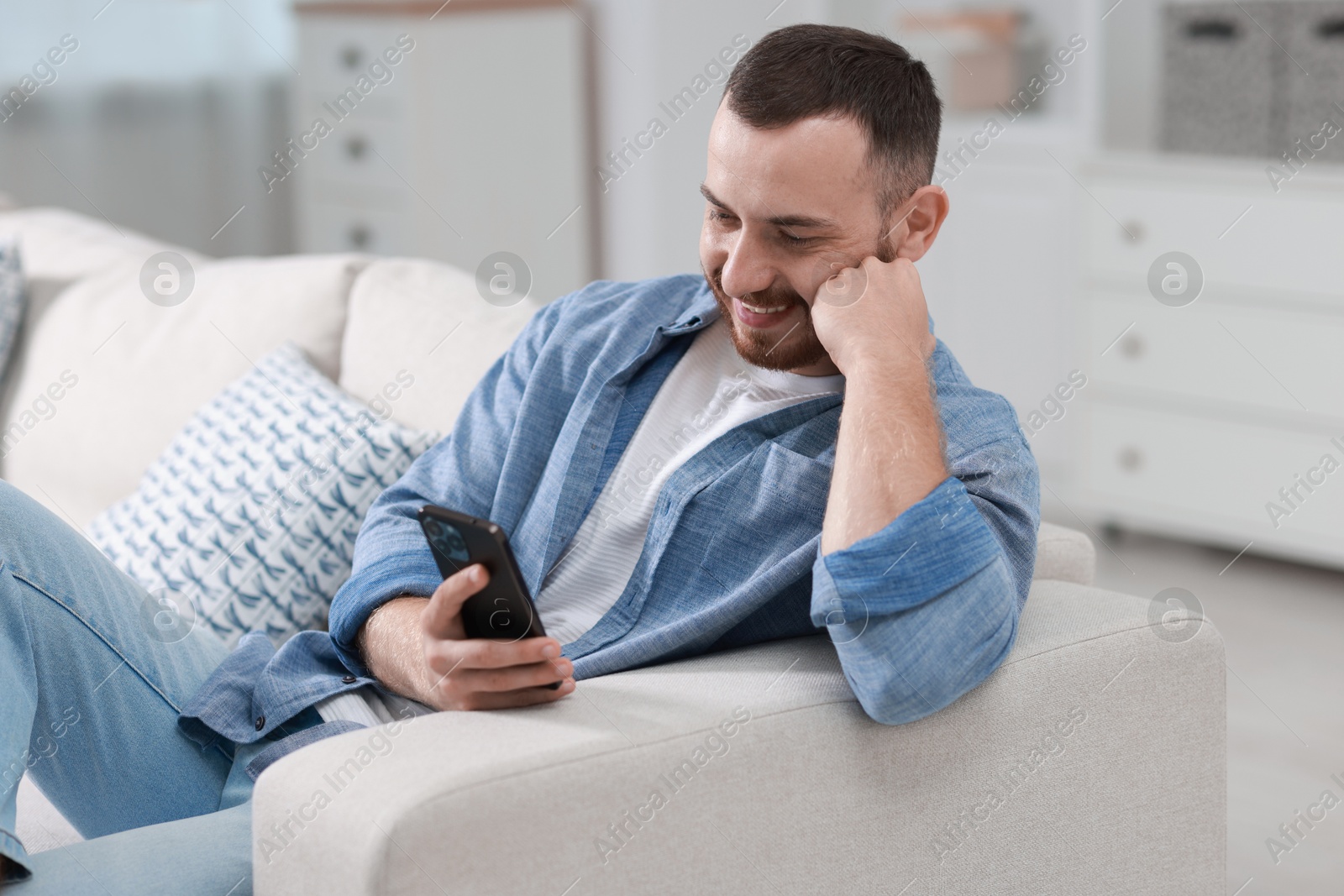 Photo of Smiling man with smartphone on sofa at home